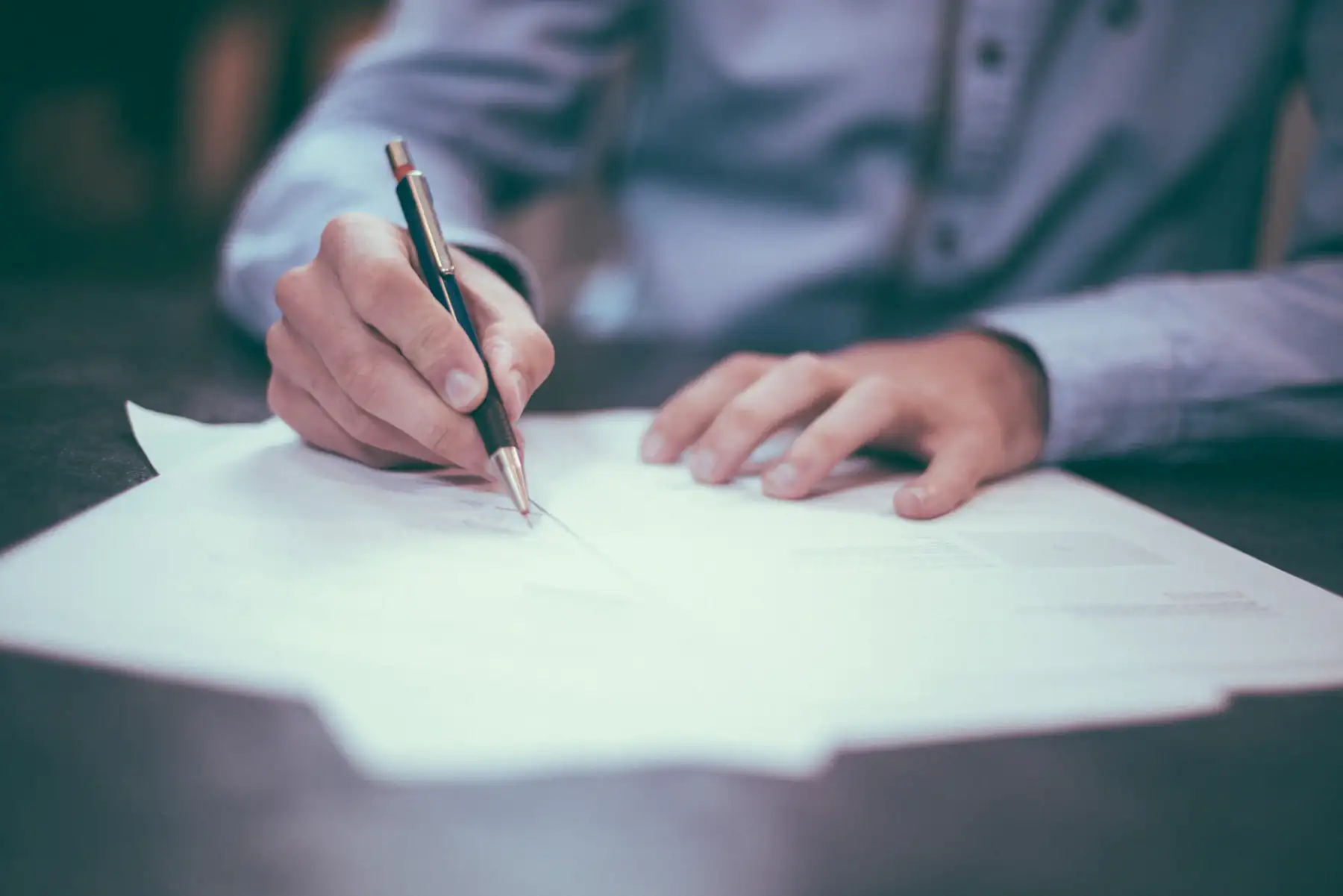 Hands signing and reviewing project paperwork at a desk